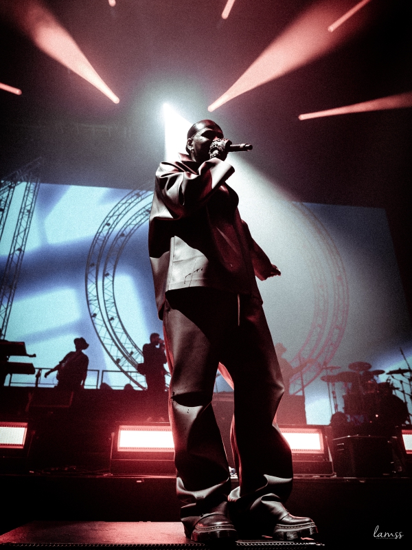 Silhouette of a singer performing on a backlit stage with large circular lighting rigs in the background. — concert photography London by Lamss Media